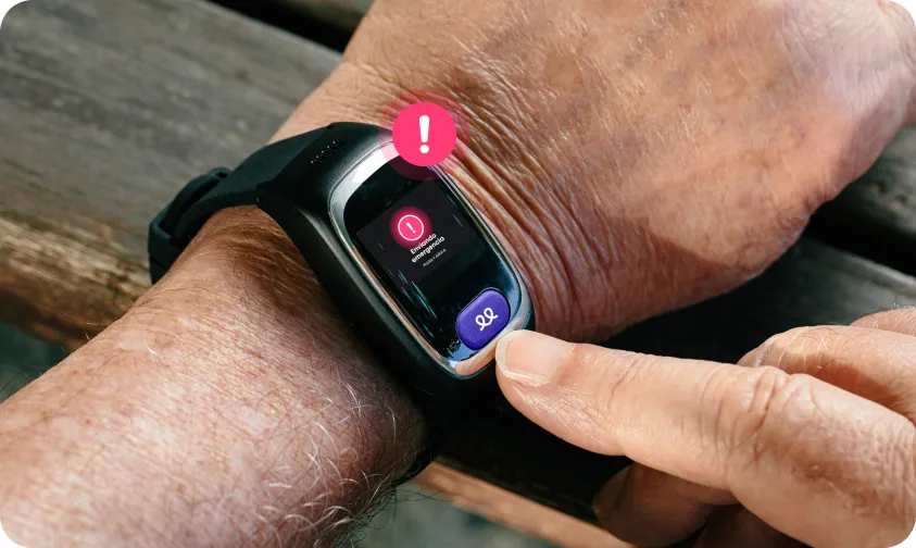 Primer plano del reloj inteligente de teleasistencia Durcal en la muñeca de una persona. La pantalla muestra un aviso de alerta roja y un botón morado de SOS, con un icono de exclamación rosa flotando sobre el dispositivo.