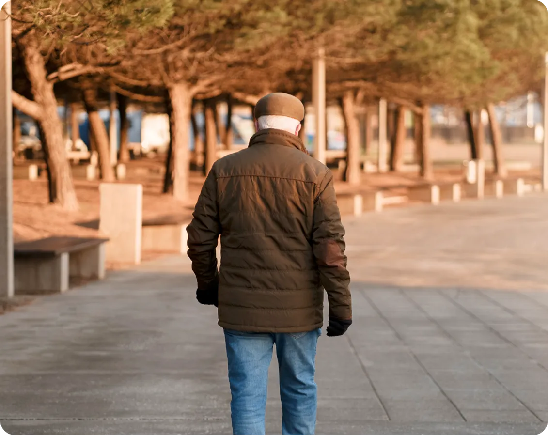 señor mayor de espaldas paseando por una calle con arboles al fondo