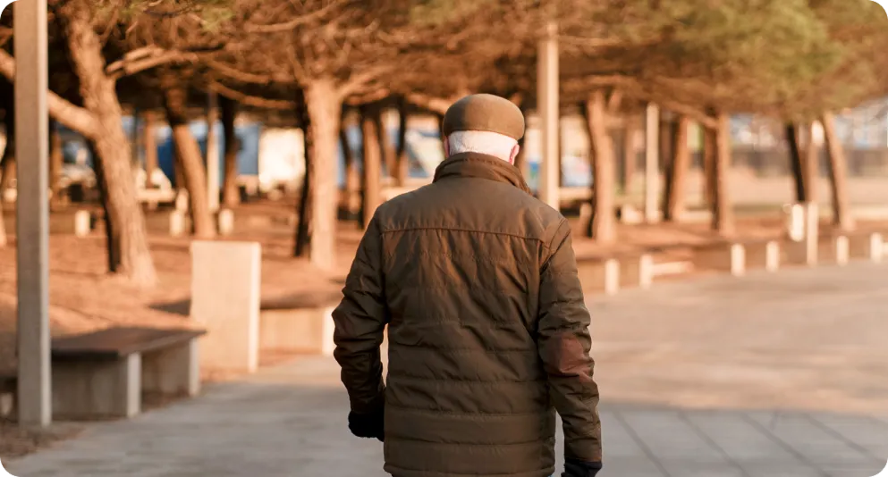 señor mayor de espaldas paseando por una calle con arboles al fondo