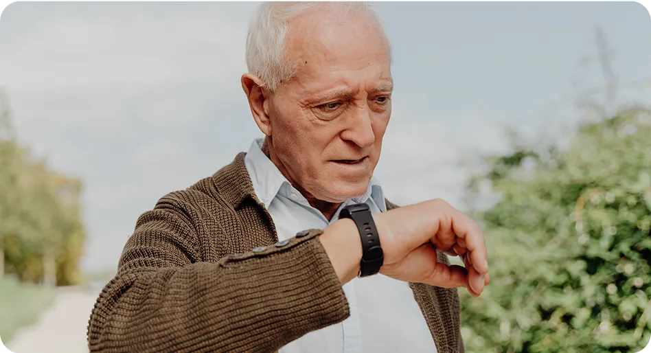 Un hombre mayor revisa la información en su smartwatch mientras está al aire libre.