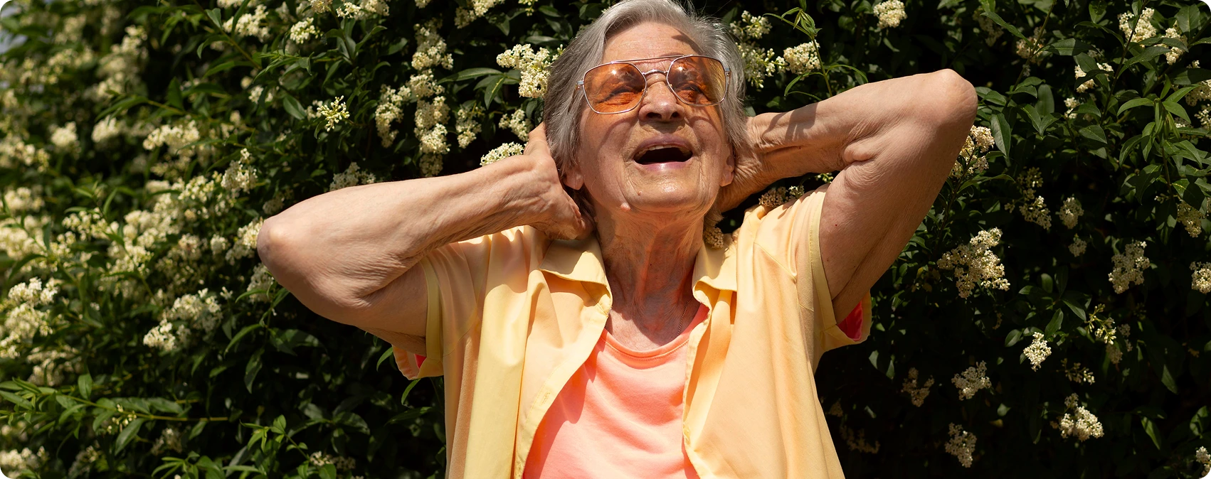 Mujer mayor feliz con gafas de sol, disfrutando al aire libre con los brazos detrás de la cabeza